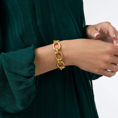 Close-up of a gold chain-link bracelet on a person wearing a dark green blouse.