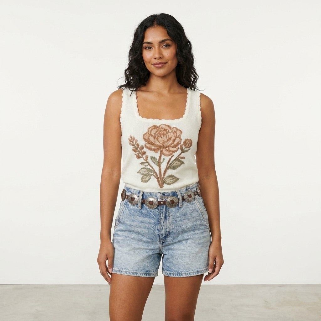Woman in floral top and denim shorts standing against a plain backdrop.
