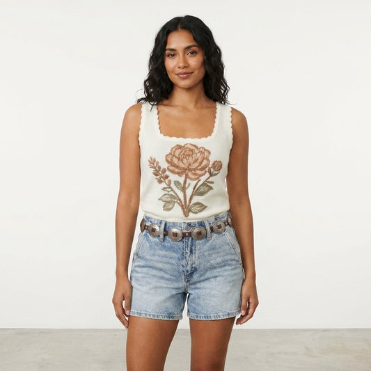 Woman in floral top and denim shorts standing against a plain backdrop.