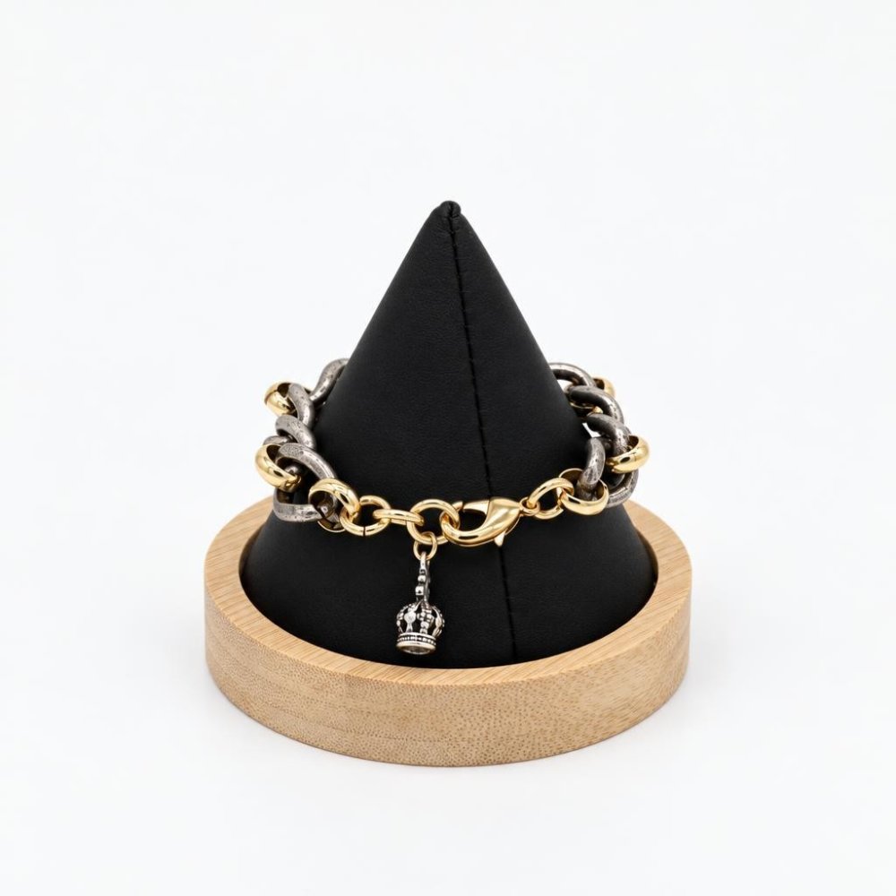 A two-tone chain bracelet with a crown charm displayed on a black stand.