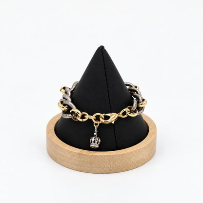 A two-tone chain bracelet with a crown charm displayed on a black stand.