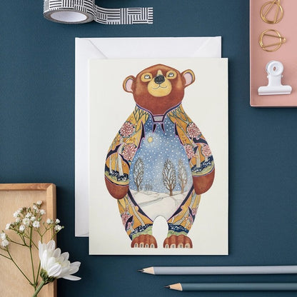 Artistic bear card with snowy landscape, on a teal background with flowers and pencils.
