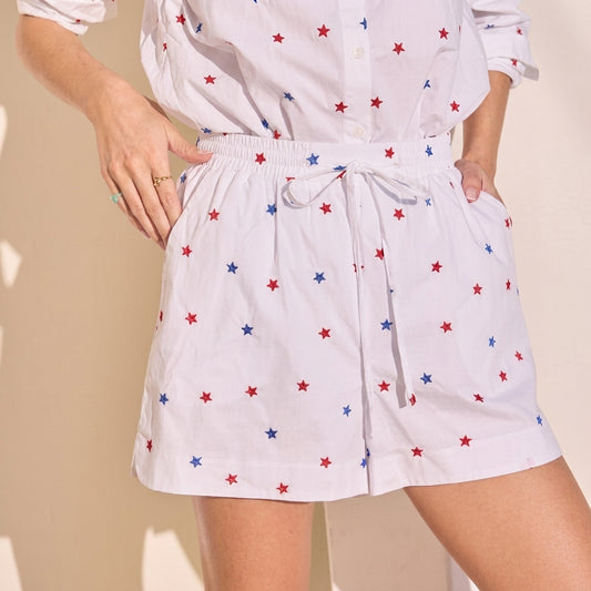 White star-patterned outfit with hands on pockets, against a beige background.