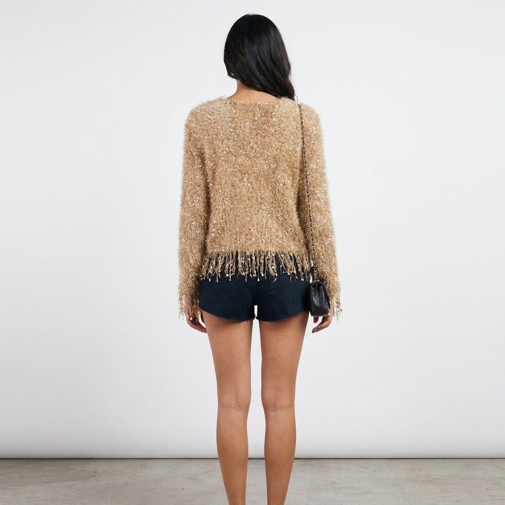 Woman in a fringed sweater and shorts, holding a black purse, facing away.