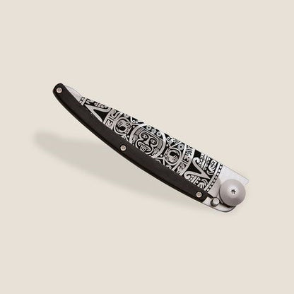 Intricately designed black and silver folding knife on a beige background.
