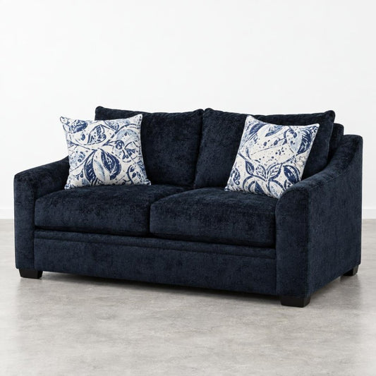 A navy loveseat with two blue-and-white patterned pillows sits against a plain white wall.