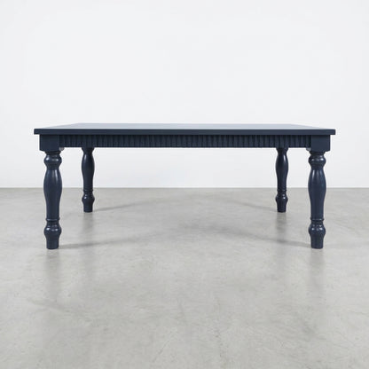 Dark blue table with carved legs on a concrete floor.