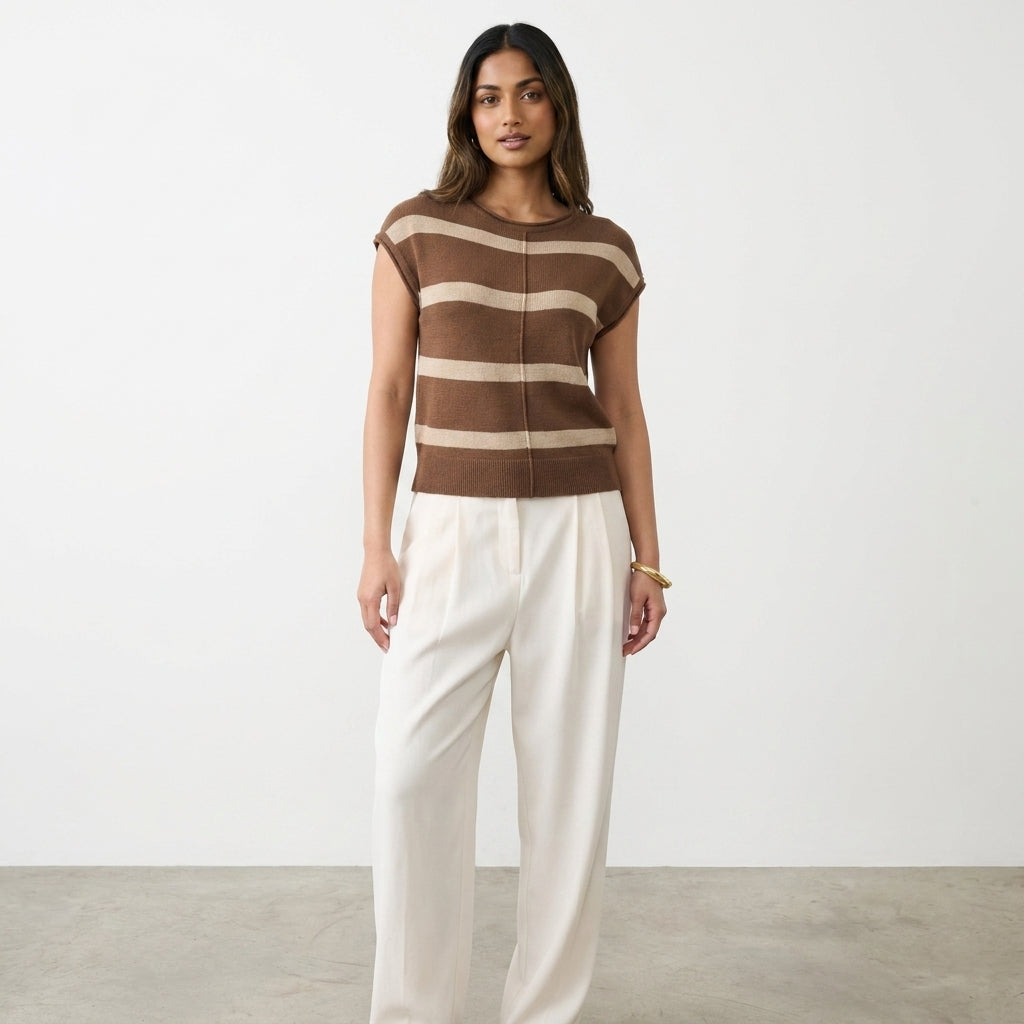 Woman in striped top and white pants against a plain backdrop.