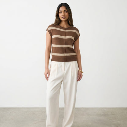 Woman in striped top and white pants against a plain backdrop.