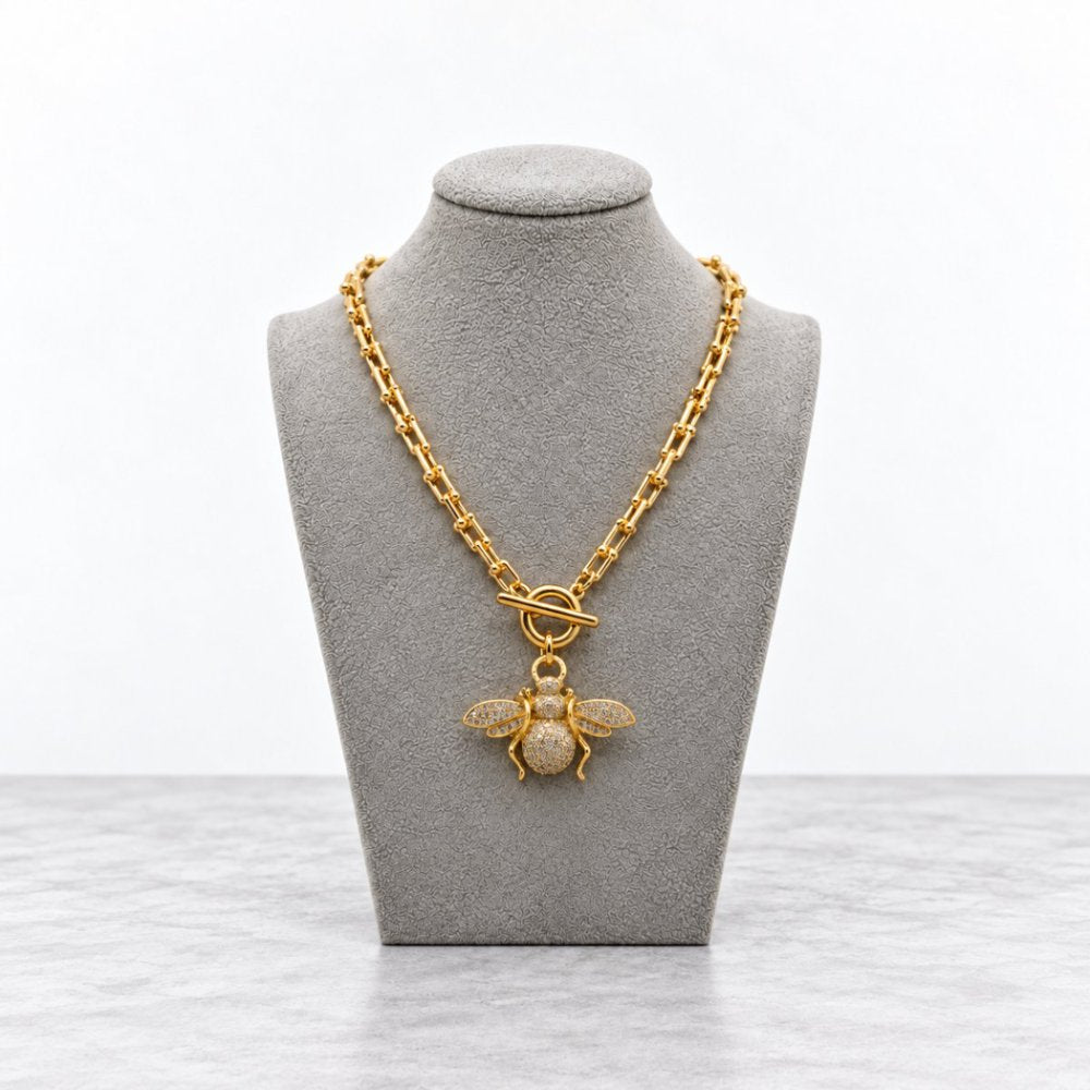 Gold chain necklace with a jeweled bee pendant displayed on a gray bust.