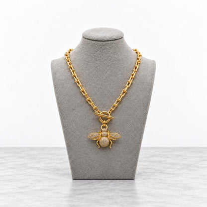 Gold chain necklace with a jeweled bee pendant displayed on a gray bust.