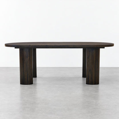 A dark wooden oval dining table with sturdy cylindrical legs in a minimalist studio.