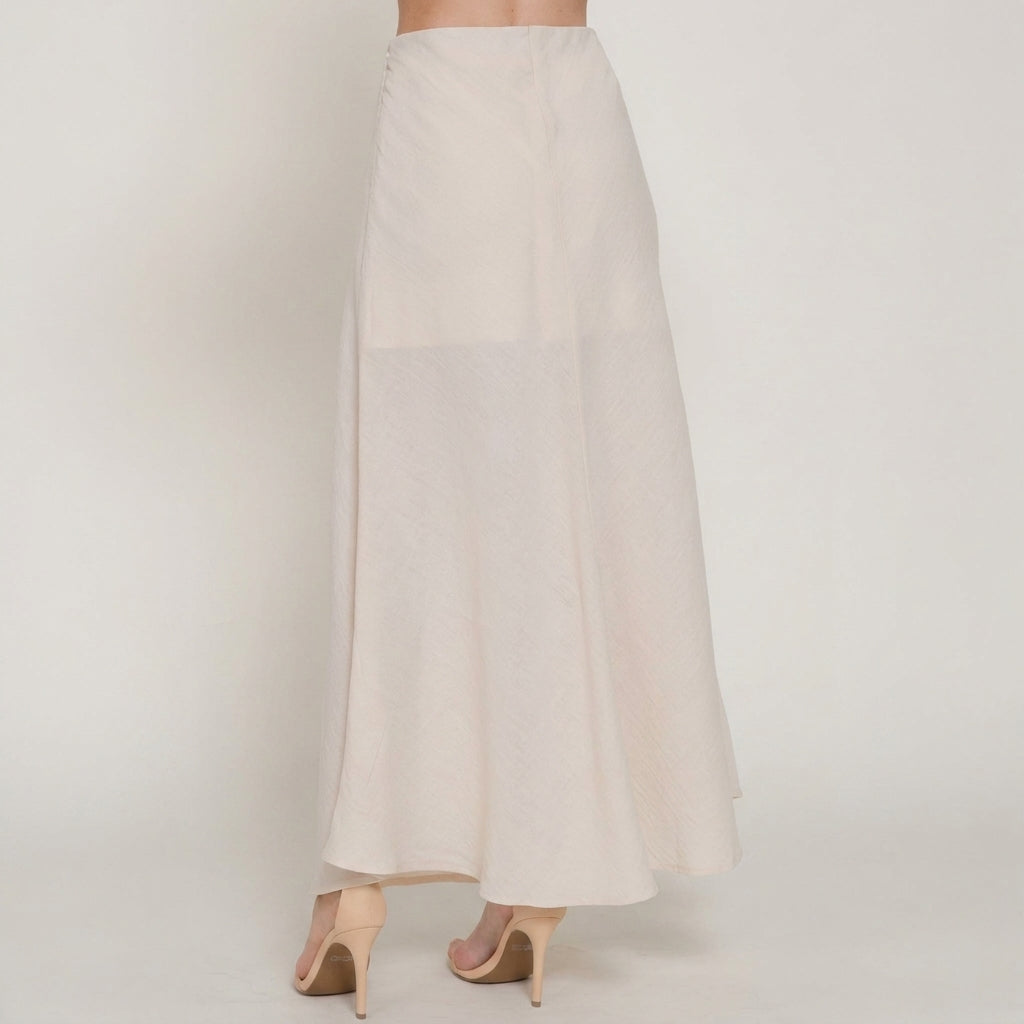 Woman in a long white skirt and nude heels, standing on a plain background.