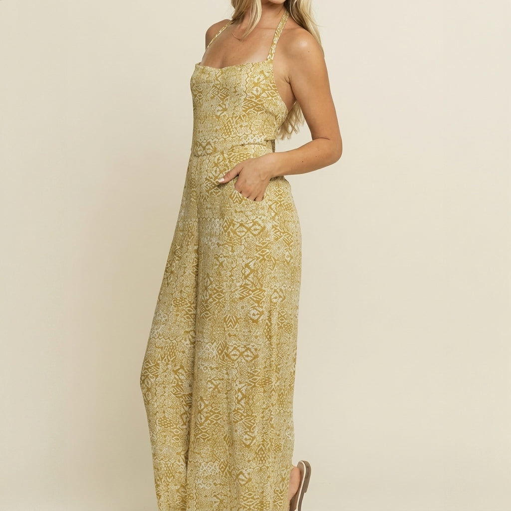 Woman in a patterned yellow halter jumpsuit, standing and smiling.