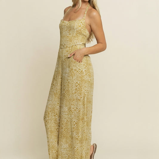 Woman in a patterned yellow halter jumpsuit, standing and smiling.
