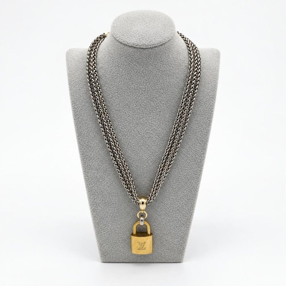 A silver chain necklace with a gold padlock pendant displayed on a gray bust.