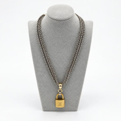 A silver chain necklace with a gold padlock pendant displayed on a gray bust.
