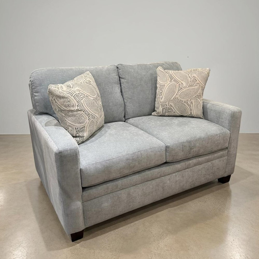 Gray sofa with two decorative pillows on a concrete floor.