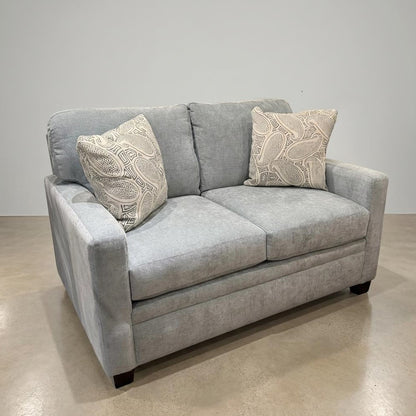 Gray sofa with two decorative pillows on a concrete floor.