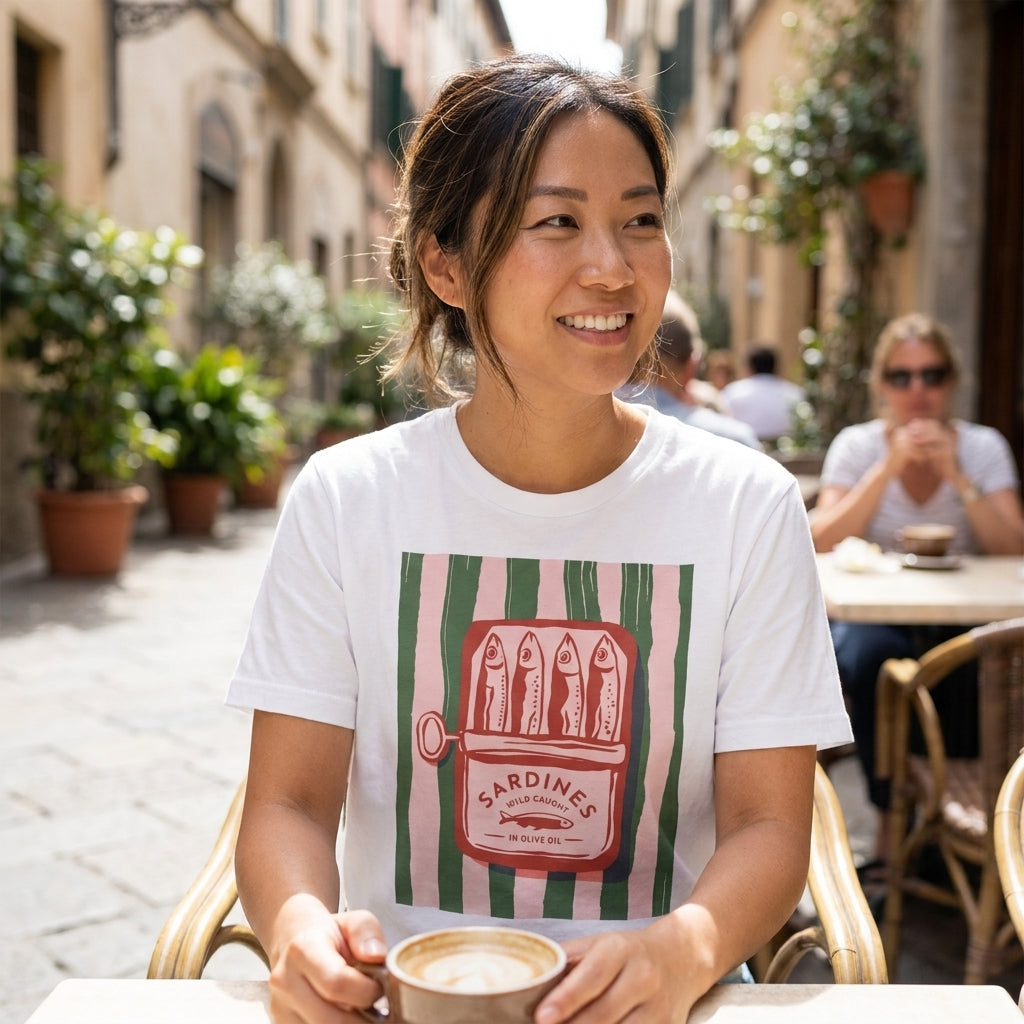 Woman with a coffee in a courtyard, wearing a sardines shirt.