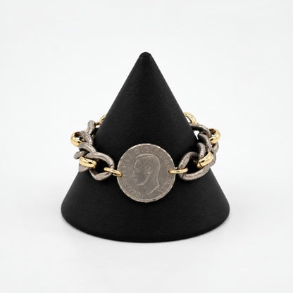 A mixed-metal chain bracelet with a vintage coin displayed on a black stand.