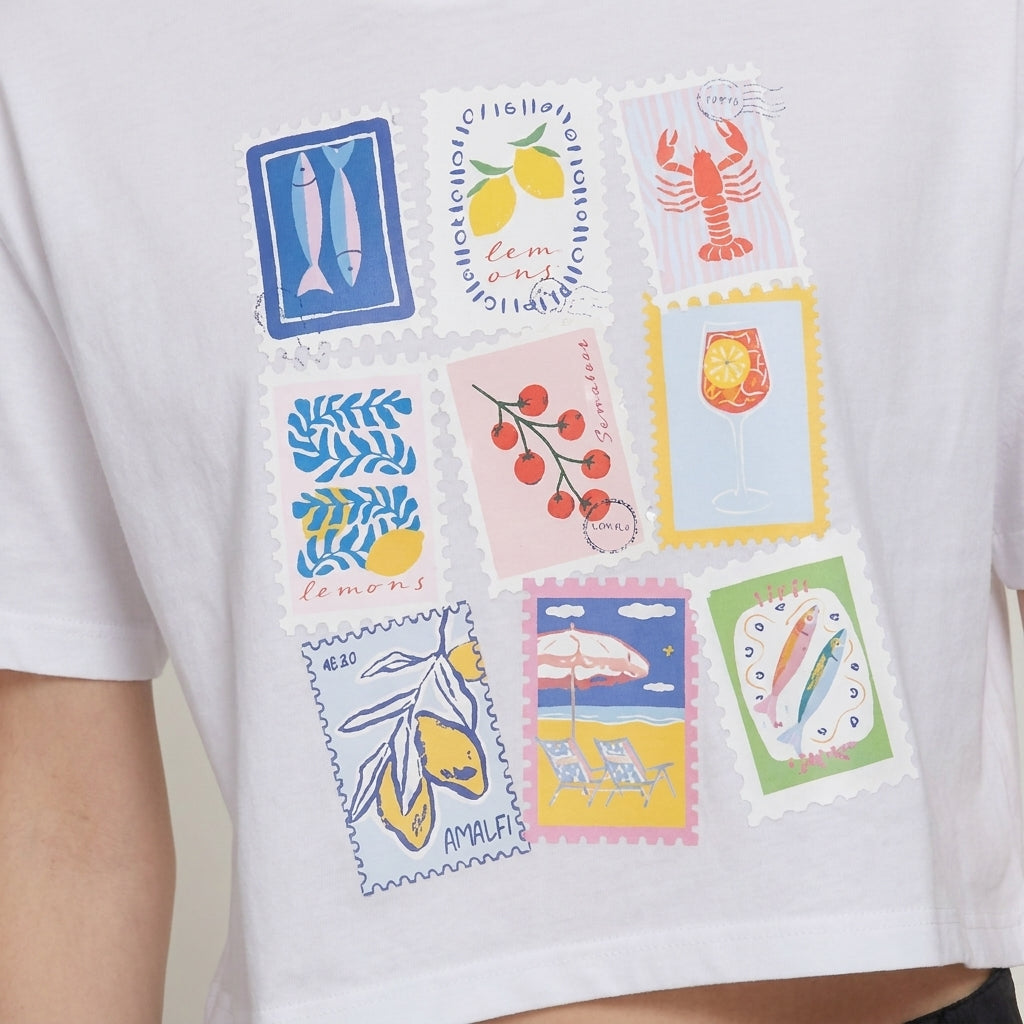 White shirt with colorful stamp designs of food and beach scenes.