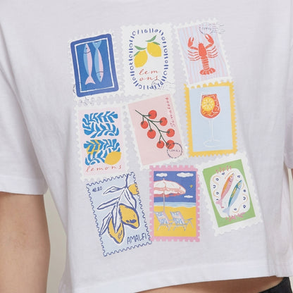 White shirt with colorful stamp designs of food and beach scenes.