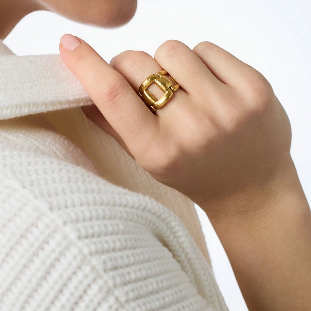 Close-up of a hand wearing a chunky gold ring against a white knitted sweater.