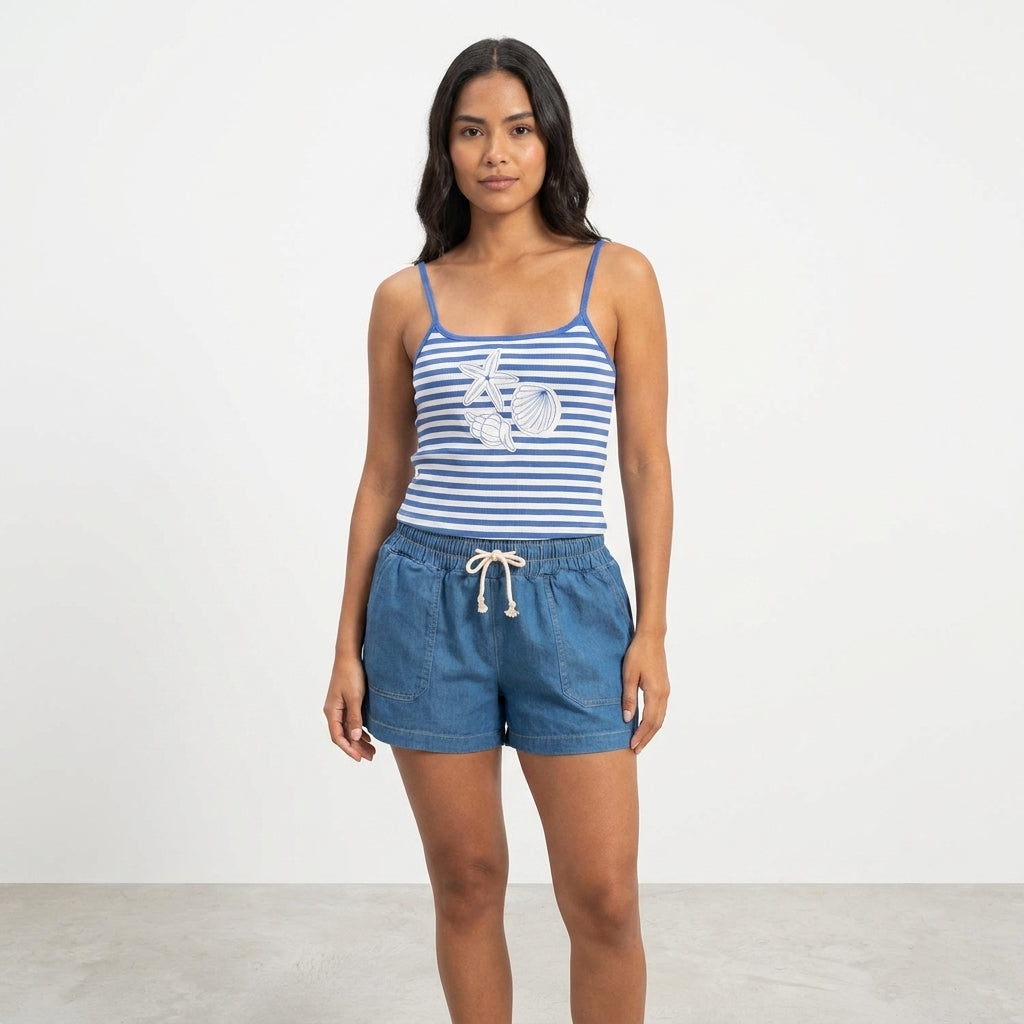 Woman in striped tank top and denim shorts stands against a plain backdrop.