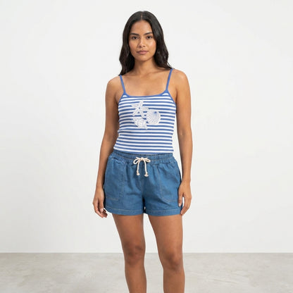 Woman in striped tank top and denim shorts stands against a plain backdrop.