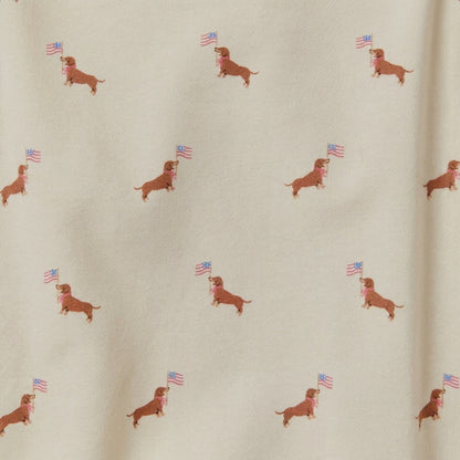 Pattern of dachshunds holding small American flags on cream fabric.