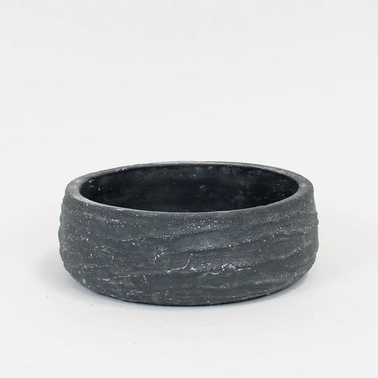 Round, textured, dark ceramic bowl on a plain background.
