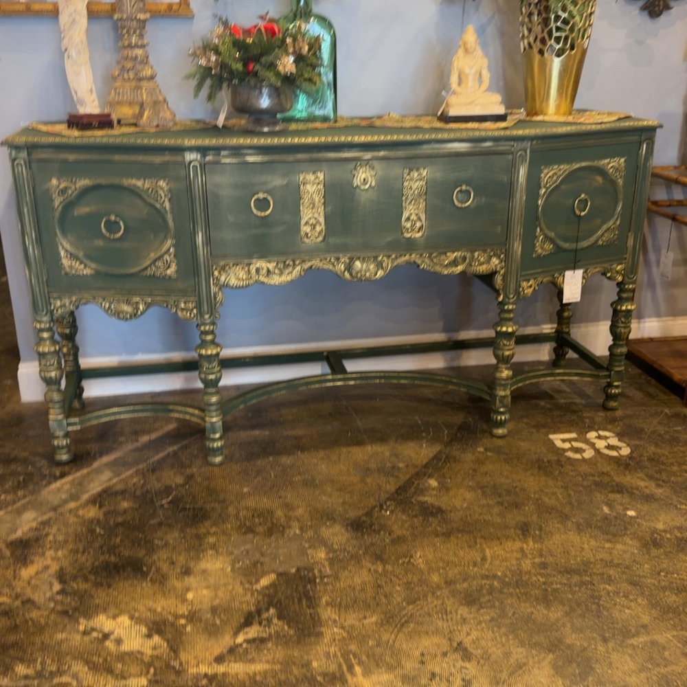 An ornate green antique sideboard with gilded details and decorative objects displayed on top.