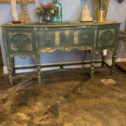 An ornate green antique sideboard with gilded details and decorative objects displayed on top.