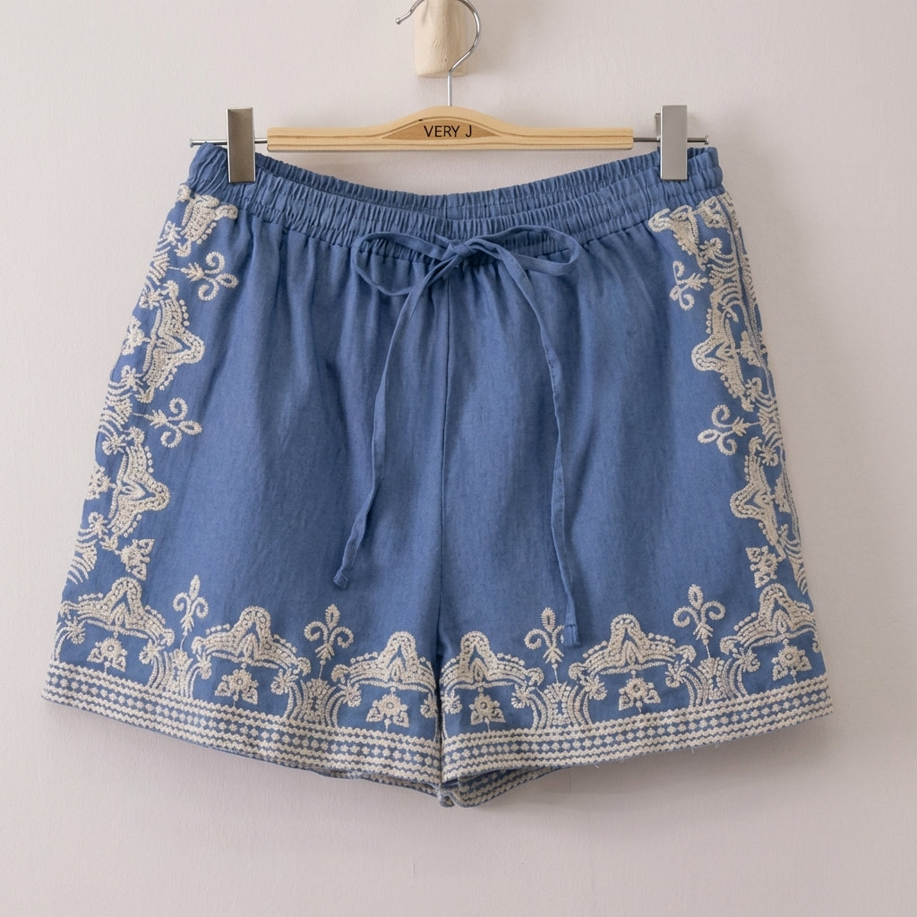 Blue shorts with white embroidery hang on a wooden hanger.