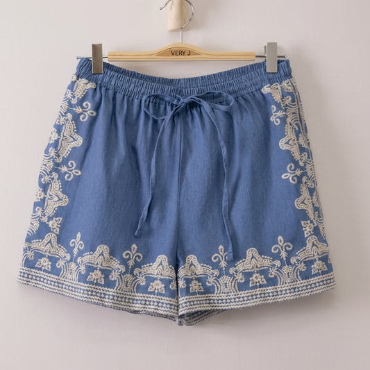 Blue shorts with white embroidery hang on a wooden hanger.