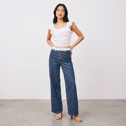 Woman in white top and jeans posing against a plain background.