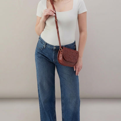 Woman in white top and jeans with a brown crossbody bag.
