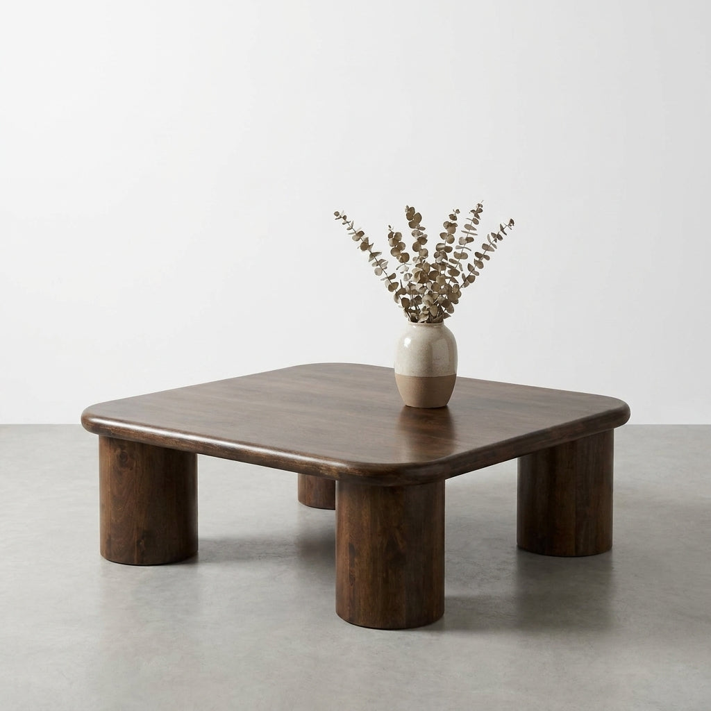 A square wooden table with a vase of dried flowers.