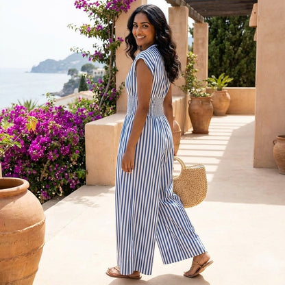 Woman in striped dress on sunny terrace by ocean, holding a straw bag.