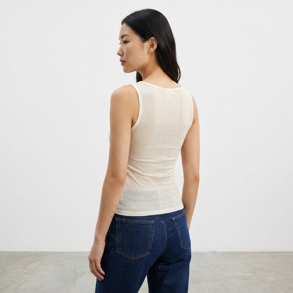 Woman in a beige tank top and jeans standing sideways.