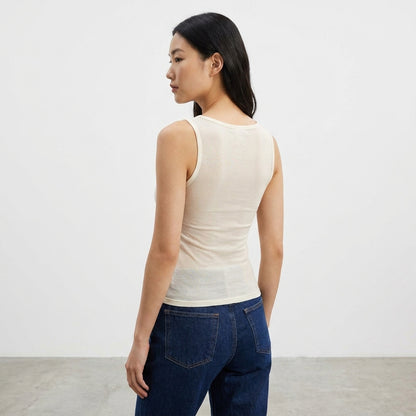 Woman in a beige tank top and jeans standing sideways.