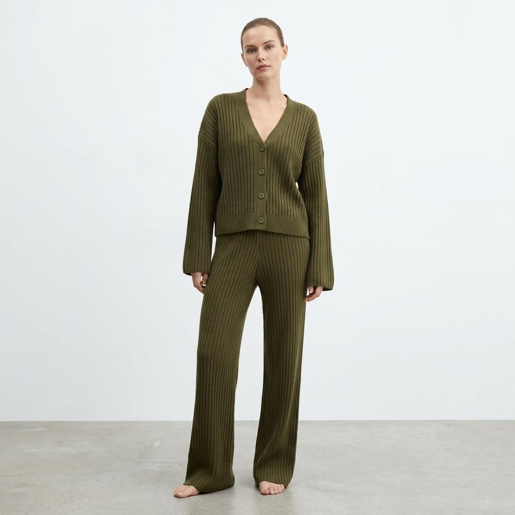 Person in a green ribbed sweater and pants, standing barefoot against a plain background.