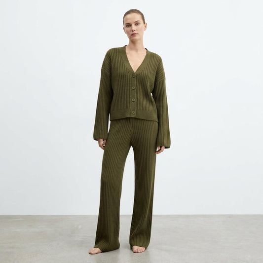 Person in a green ribbed sweater and pants, standing barefoot against a plain background.