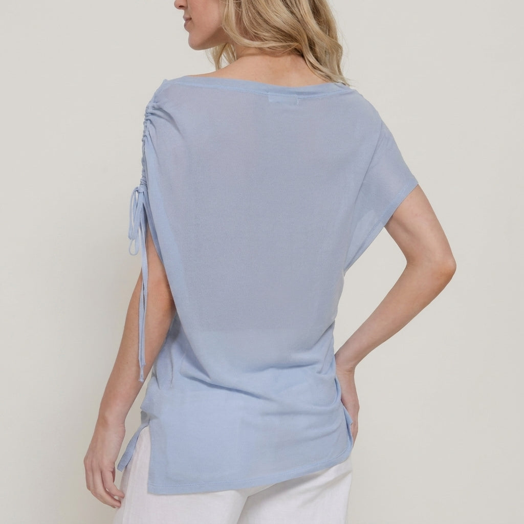 Woman in a light blue top with ruched sleeves, standing sideways.