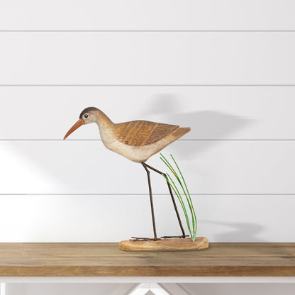 Wooden bird sculpture on a wooden shelf, white shiplap background.