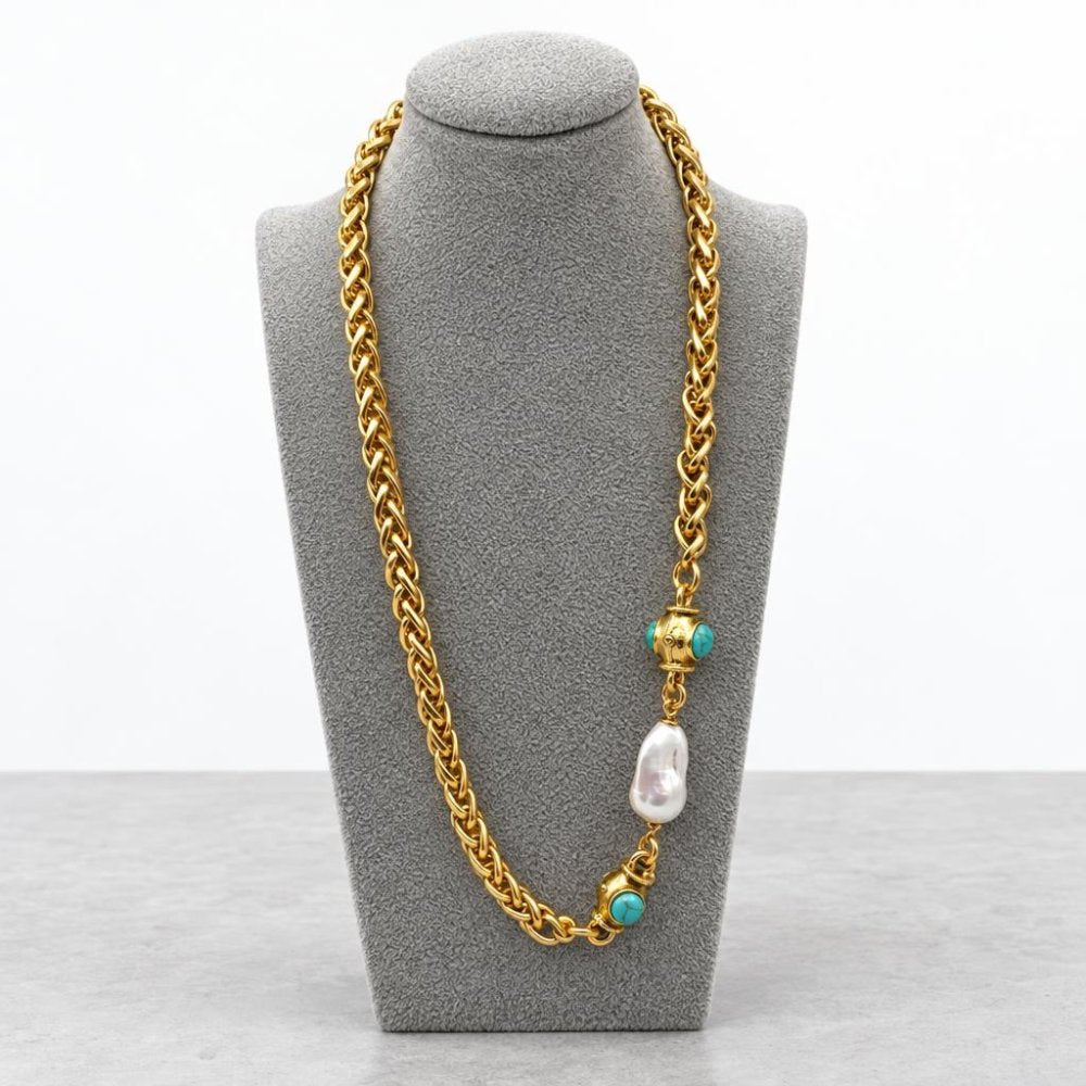 Gold chain necklace with turquoise accents and a pearl, displayed on a gray stand.