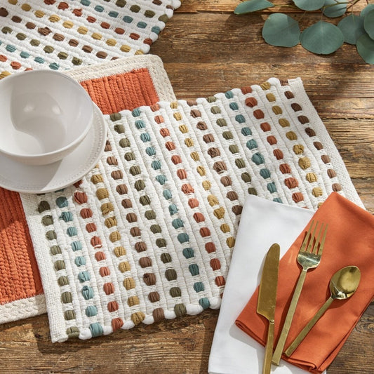 Colorful placemats, white bowls, and gold cutlery on a wooden table.