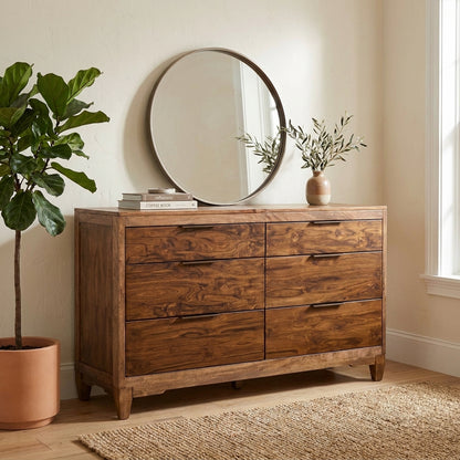 Wooden dresser with round mirror, potted plant, and books.