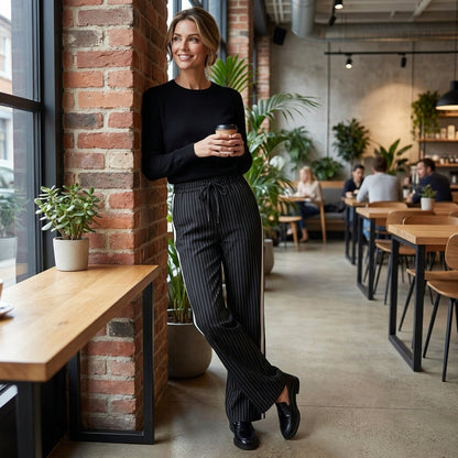 Person in café smiling, holding a coffee cup, standing by a window and brick wall.